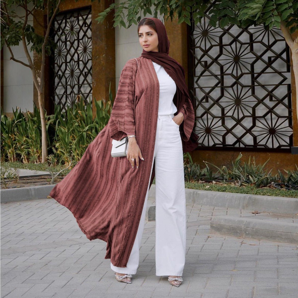 Woman wearing a vintage knitted longline open front cardigan abaya in mauve with white trousers.
