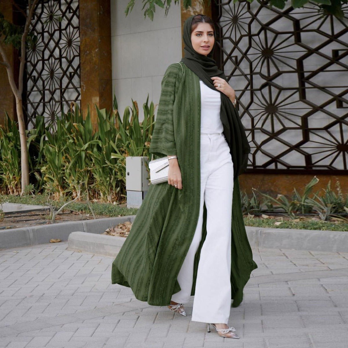 Woman wearing a long olive green vintage knitted cardigan abaya over a white top and trousers.