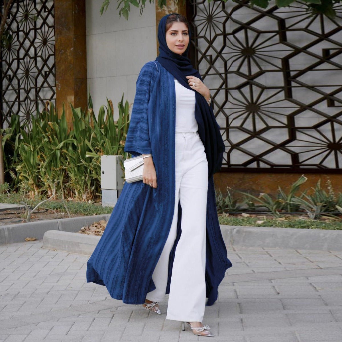 Woman wearing a blue vintage knitted longline open front abaya over a white top and wide-leg pants.