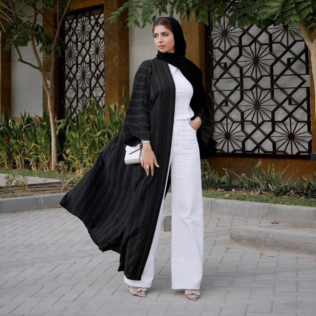 Woman wearing a black vintage knitted longline open front abaya over a white top and wide-leg pants.