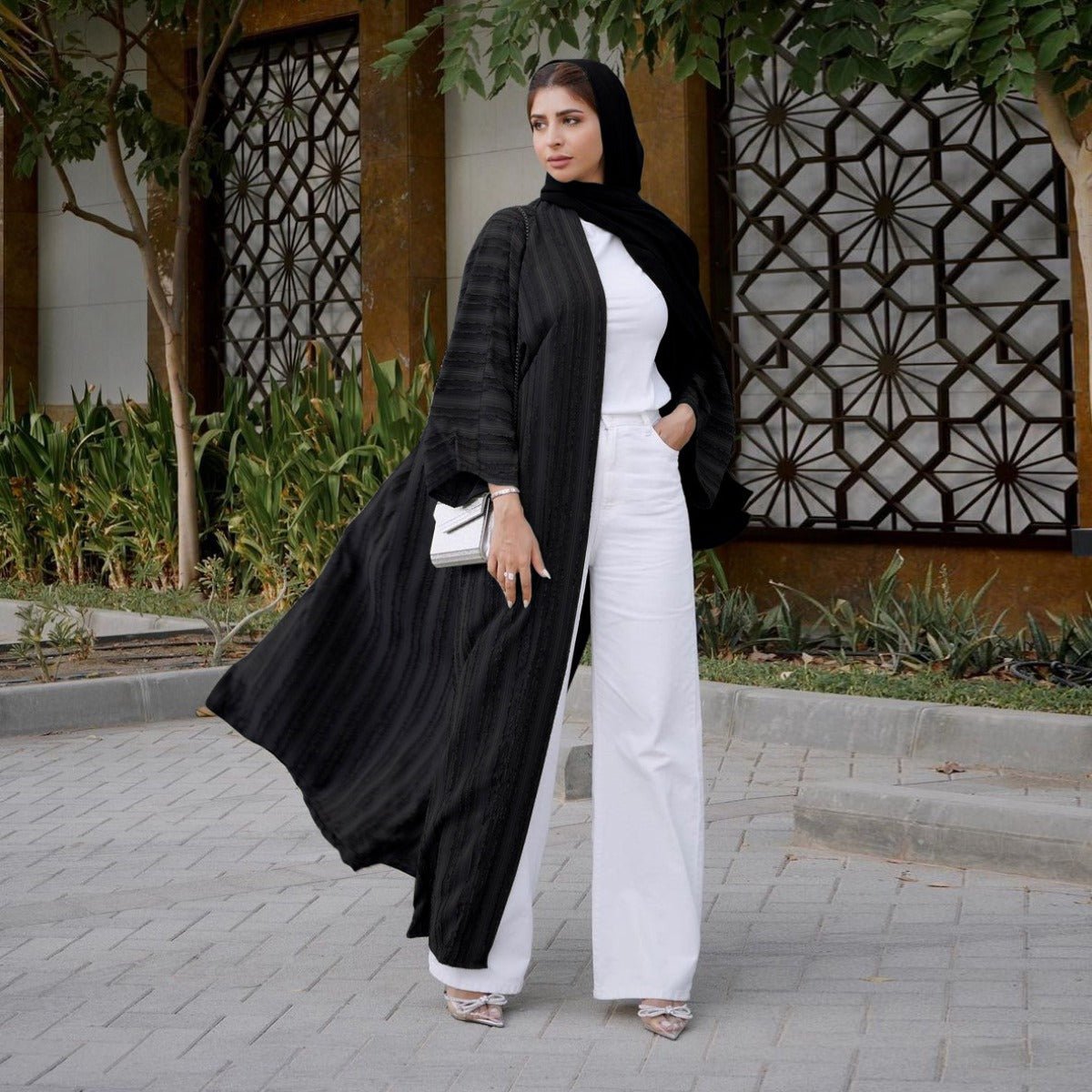 Woman wearing a black vintage knitted longline open front abaya over a white top and wide-leg pants.
