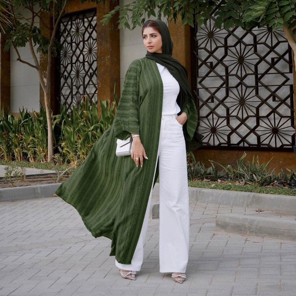 Woman wearing a green vintage knitted longline open front cardigan abaya over white pants and top.