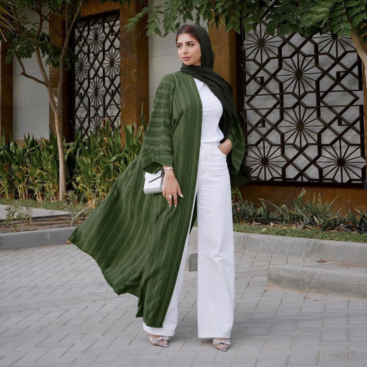 Woman wearing a green vintage knitted longline open front cardigan abaya over white pants and top.