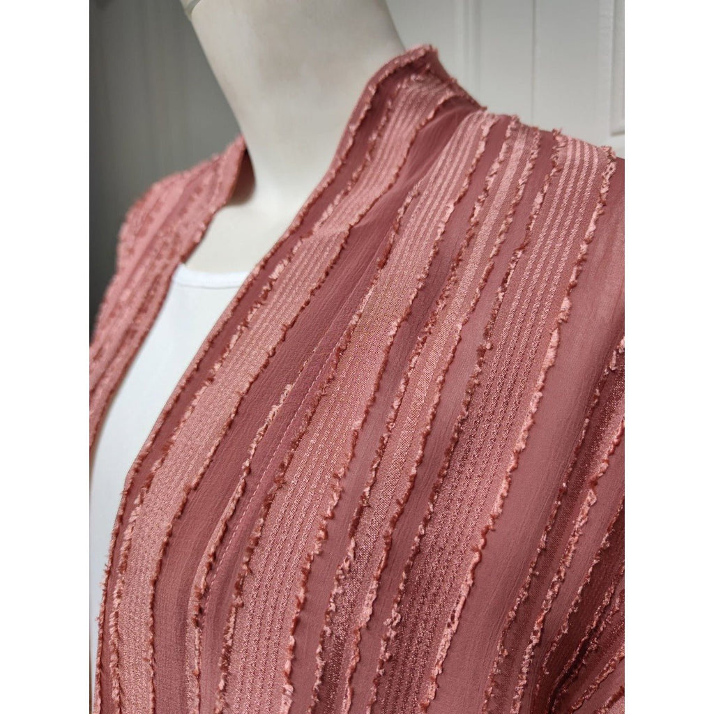 Close-up of a dusty rose open-front cardigan with vertical textured stripes and fringe details.