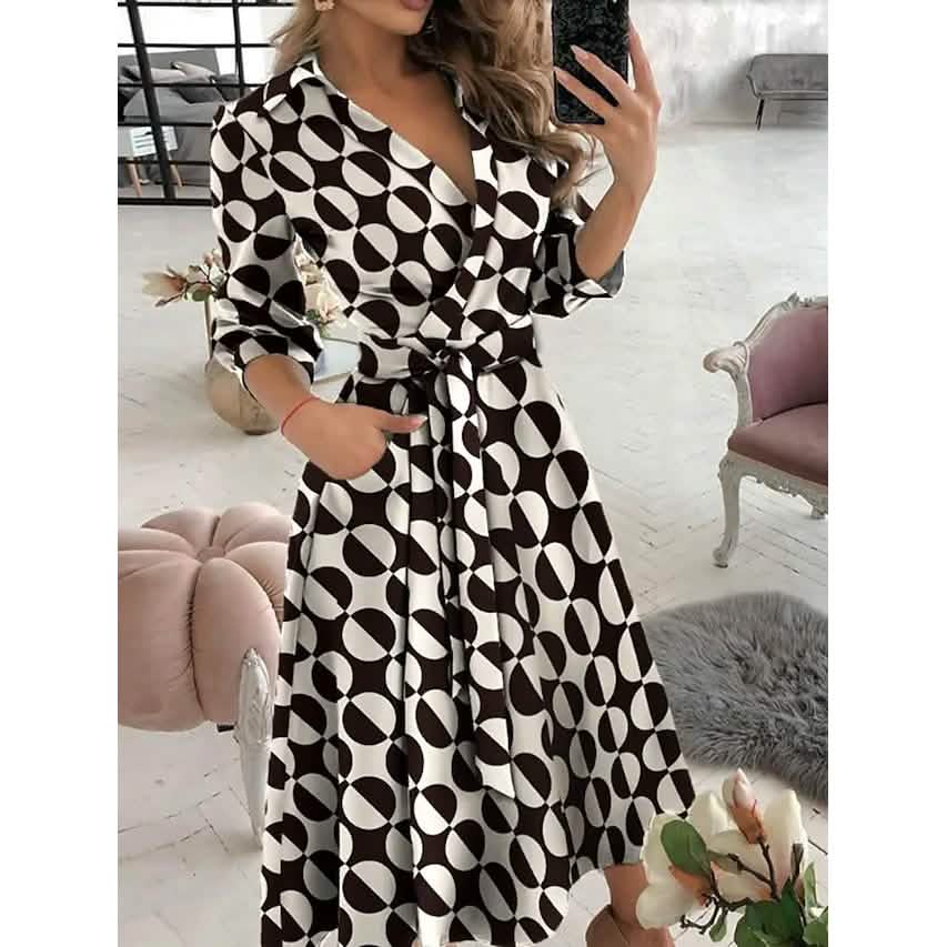 Woman wearing a brown and white geometric print A-line midi dress with a V-neck and tie waist.