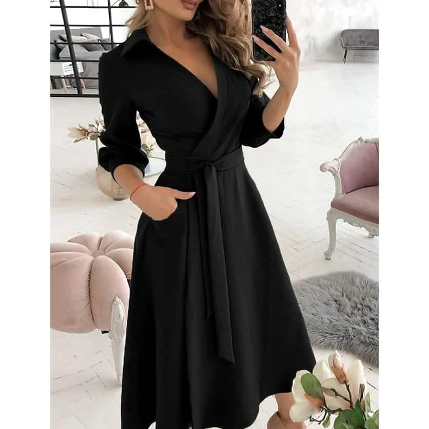 Woman wearing a black A-line midi dress with a V-neck and tie belt.