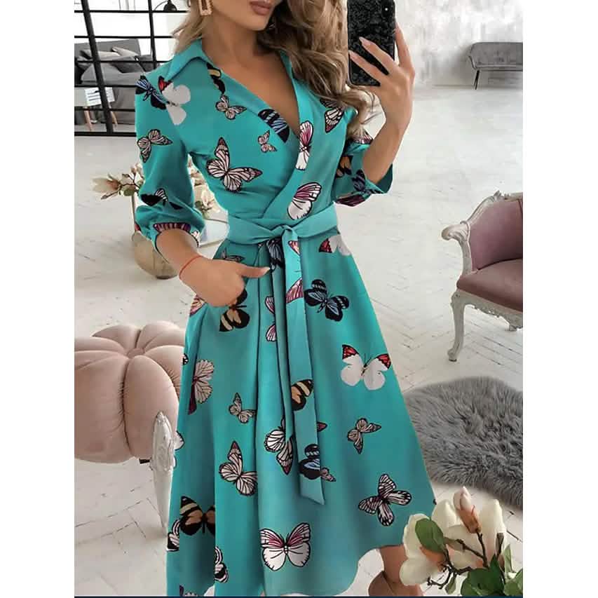 Woman wearing a teal A-line midi dress with a butterfly print and a tie belt.