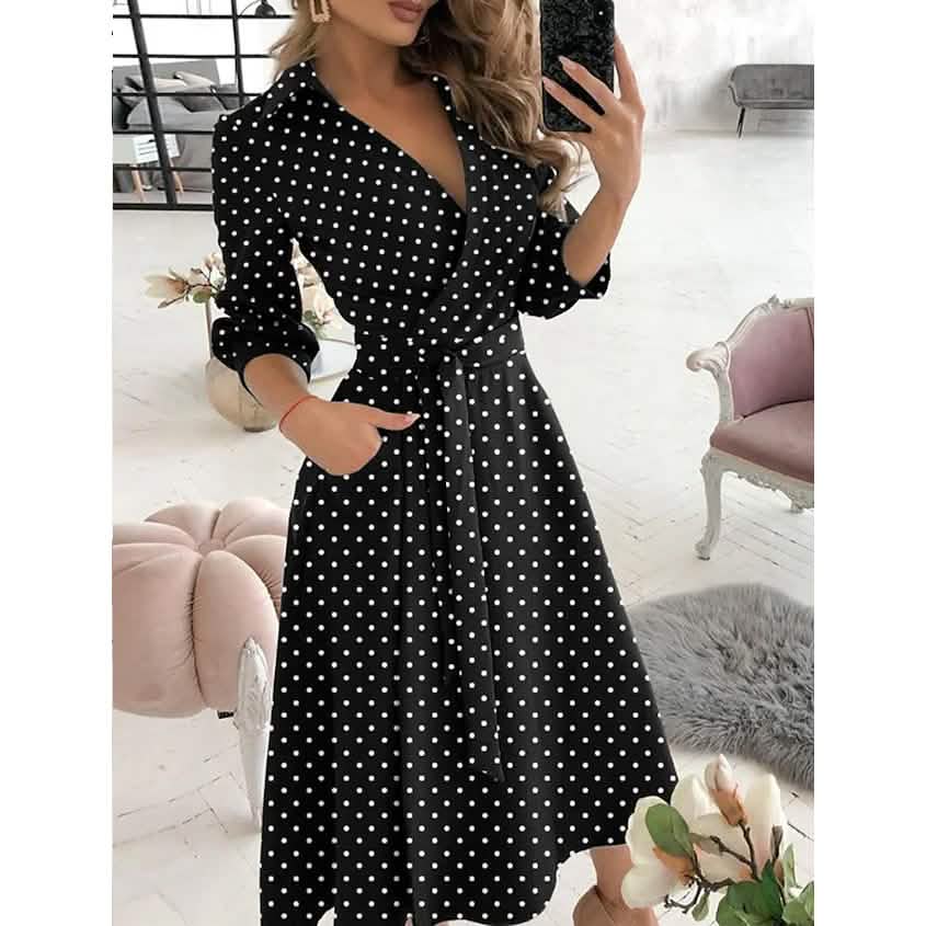 Woman wearing a black A-line midi dress with white polka dots and a V-neck.